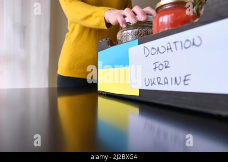 Eine unkenntliche Frau, die Dosen mit Lebensmitteln für ukrainische Flüchtlinge in die Kiste legt Stockfoto