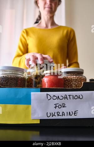 Eine unkenntliche Frau, die Dosen mit Lebensmitteln in eine Schachtel legte, um ukrainischen Flüchtlingen zu spenden. Stockfoto