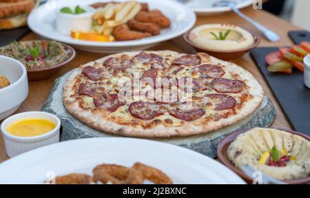 Pepperoni Pizza mit anderen arabischen Gerichten auf dem Tisch. Stockfoto