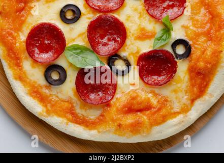 Nahaufnahme einer Pepperoni-Pizza mit schwarzen Oliven und Basilikumblättern. Stockfoto