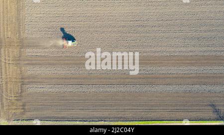Oben Ansicht des Traktors als Zugmaschine, erschütterndes Ackerfeld, Vorbereitung der Erde für die Pflanzung neuer Ernte in der nächsten Saison. Die Staubwolke fliegt hinter sich her Stockfoto