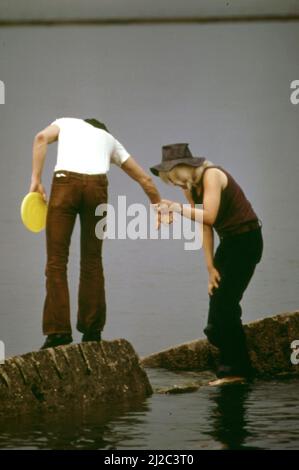 Ein Paar, das im Lincoln Park ein Frisbee-Spiel spielt, macht sich auf den Felsen der Küste des Lake Michigan auf den Weg. 1973 Stockfoto