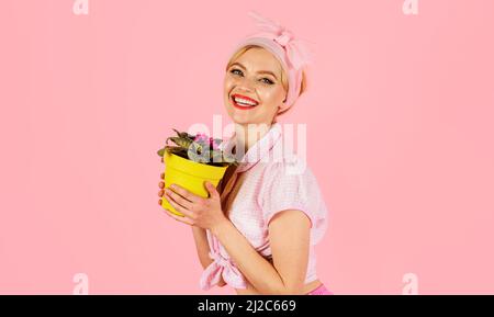 Lächelndes Mädchen mit blühender afrikanischer violetter Blume saintpaulia im Topf. Frau, die Blumen kultiviert. Stockfoto