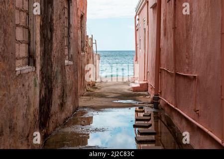 Blick auf das Karibische Meer durch verwitterte rot gestrichene Häuser in Willemstad, Curacao Stockfoto