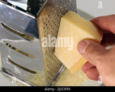 Männliche Hand Reibe Parmesan Käse auf einer Metallküchenreibe, Nahaufnahme der Verwendung einer Reibe Stockfoto