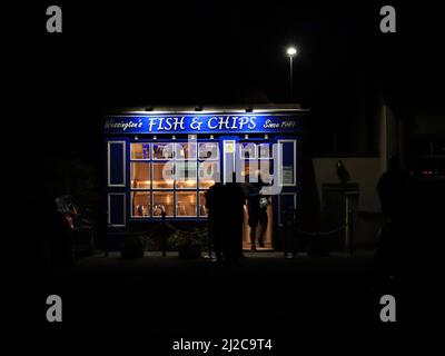 Im kleinen Dorf Wessington in Derbyshire Dales verlässt ein Kunde einen beliebten und gebrauchten bunten Fisch- und Chipshop zu seinem Abendessen. Stockfoto