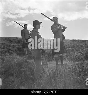 Frau mit einer Schrotflinte und zwei Männer im Kilt ca. 1930s-1950s Stockfoto