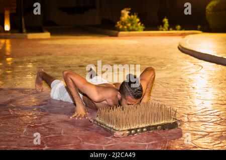 Schauspieler Fakir Stuntman legt das Gesicht auf ein Nagelbett, ohne verletzt zu werden. Stockfoto