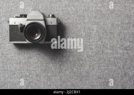 Analoge Retro-Kamera. Vintage altmodische Kamera mit Objektiv auf grauer Leinwand. Draufsicht. Stockfoto