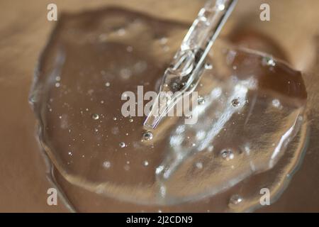 Nahaufnahme der Glaspipette im transparenten Kosmetikgel.Metallischer Hintergrund. Stockfoto