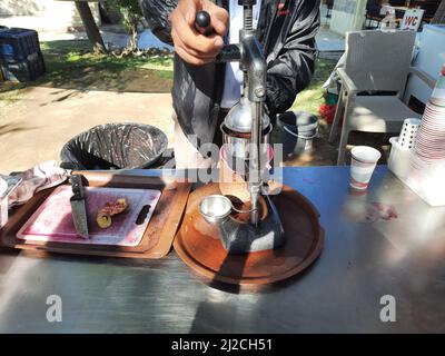 Verkäufer mit Entsafter, der frischen Granatapfelsaft auf einem Straßenmarkt an einem sonnigen Tag im Freien zubereitet. Stockfoto