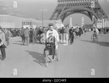 Frau im Rollstuhl auf dem Messegelände. Im Hintergrund der Eiffelturm ca. 1937 Stockfoto