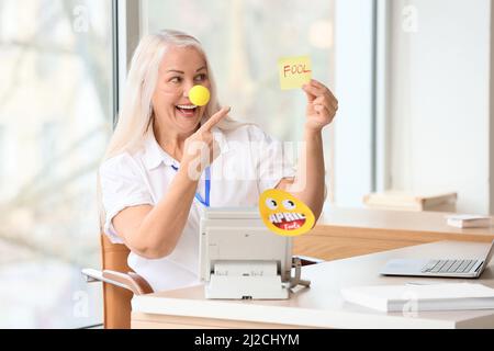 Lustige reife Frau mit Clownnase und klebrigem Papier im Büro. April Narren Tag Feier Stockfoto