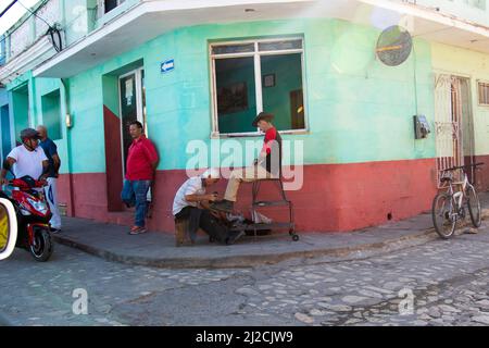 Ein Mann in Trinidad, Kuba, bringt ein Paar Cowboy-Stiefel auf einen Cowboy, während die Menschen durch die Straße der Stadt gehen. Stockfoto