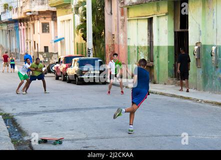 Der junge Mann schlägt und spielt mit einem Tennisball und seinen Freunden auf einer Straße in Havanna, Kuba, vor einem Skateboard auf der Straße. Stockfoto