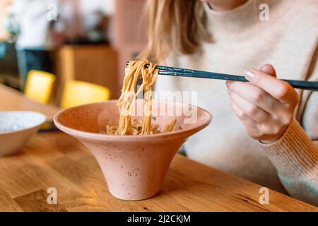 Ansicht einer Frau, die von Hand Nudeln mit Essstäbchen isst Stockfoto