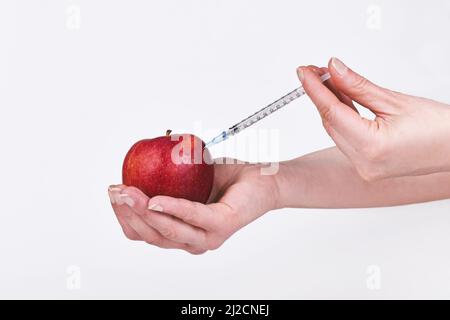 Apfelfrucht wird mit einer Spritze injiziert. Von weiblicher Hand gehalten. Stockfoto