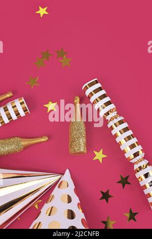 Partyhüte, kleine goldene Champagnerflaschen, Sternkonfetti und Geschenke auf rosa Hintergrund Stockfoto
