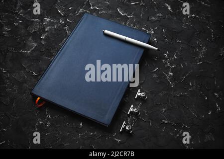 Leerer blauer Notizblock, Stift und Clips auf schwarzem Gips-Hintergrund. Stockfoto