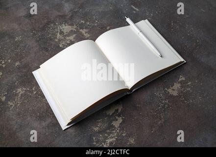Foto des geöffneten Buches mit leeren weißen Seiten und Stift auf konkretem Hintergrund. Stockfoto