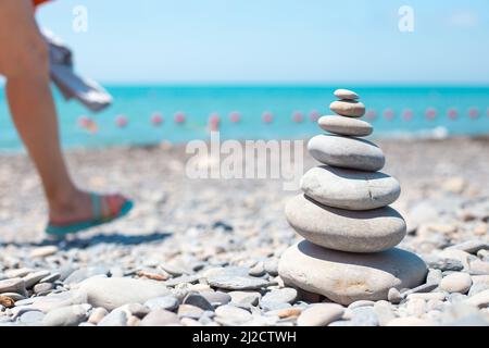 An der Küste, wo die Touristen spazieren, werden runde Steine übereinander von einer Pyramide gestapelt. Urlaubsbilanz-Konzept. Stockfoto