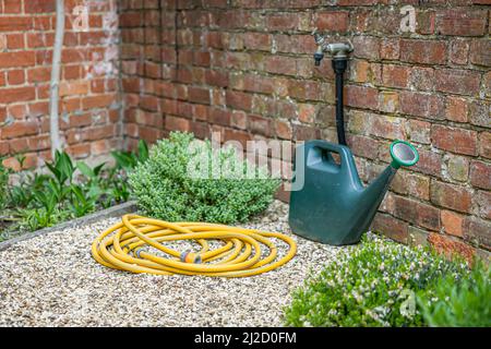 Gießkannen, Gartenschlauch (Schlauchleitung) und Außenhahn in einem Garten im britischen Garten. Gärtnerszene Stockfoto