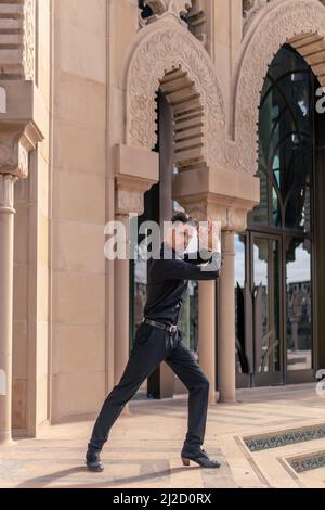 der spanische Flamenco-Tänzer posiert in schwarzer Kleidung und klatscht mit den Händen vor einem Bogen im Mudejar-Stil Stockfoto