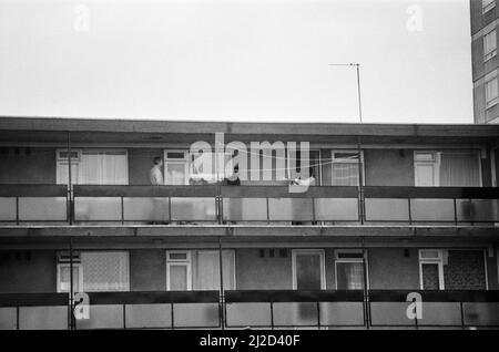 Errol Walker zwang sich am 25.. Dezember 1985 in eine Wohnung im dritten Stock des Poynter Court. Eine Frau taumelte aus und starb später an Messerstichen. Am folgenden Tag umzingelten bewaffnete Polizisten die Wohnungen, in denen Walker ein vierjähriges Mädchen als Geisel hatte, als die Belagerung fortgesetzt wurde. Auf dem Bild droht Walker mit einem Küchenmesser Polizeivertretern, die versuchen, mit ihm zu sprechen. 26.. Dezember 1985 Stockfoto