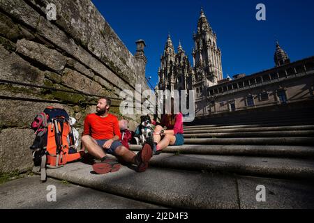 Zwei Pilger beenden den Camino de Santiago und ruhen sich auf den Stufen der Plaza del Obradoiro vor der Kathedrale von Santiago de Compostela aus Stockfoto