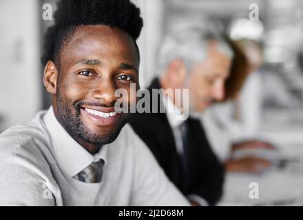 Der richtige Zeitpunkt ist jetzt. Porträt eines Geschäftsmannes, der in einem Sitzungssaal sitzt und im Hintergrund verschwommene Kollegen hat. Stockfoto