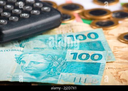 Finanzierungskonzept. Einhundert-reais-Banknoten mit Taschenrechner und Münzen. Brasilianisches Geld. Stockfoto