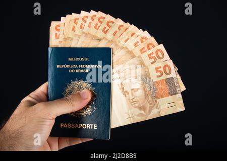 Hand hält brasilianischen Pass mit fünfzig reais Banknoten. Brasilianisches Geld. Stockfoto