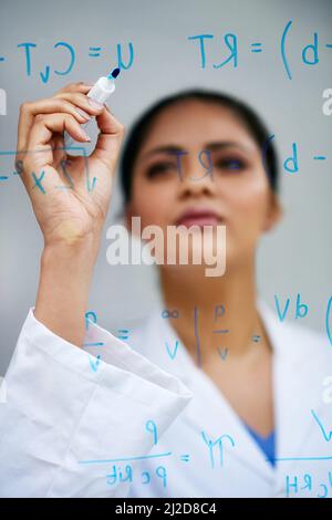 Shell löst dieses Problem. Ausgeschnittene Aufnahme einer attraktiven jungen Wissenschaftlerin, die in ihrem Labor an einer Glaswand arbeitet. Stockfoto