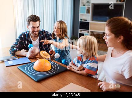 Waren zusammen durch das Universum unterwegs. Aufnahme einer schönen jungen Familie, die zu Hause an einem wissenschaftlichen Projekt arbeitet. Stockfoto