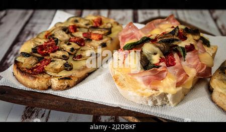 Große Bruschettas mit Käse, Pilzen, Prosciutto und Tomaten in verschiedenen Kombinationen. Mediterranes Speisekonzept. Stockfoto