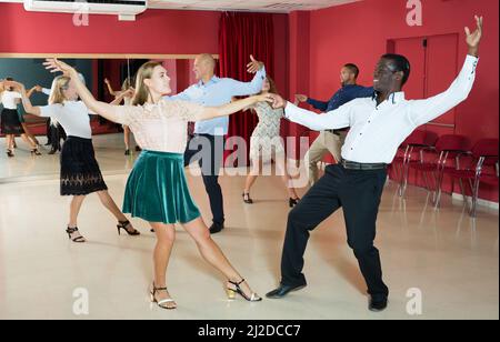 Junge Leute, die lindy tanzen, hüpfen paarweise in einem modernen Tanzsaal Stockfoto