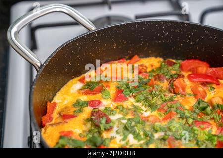 Spiegelei mit Gemüse und Kräutern in schwarzer Bratpfanne auf weißem Herd. Seitenansicht Stockfoto