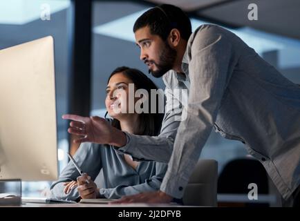 Das Geschäft geht weiter, wenn die Mitarbeiter sich mit der Arbeit abfinden. Aufnahme eines jungen Mannes, der seinem Kollegen in einem Callcenter spät in der Nacht hilft. Stockfoto