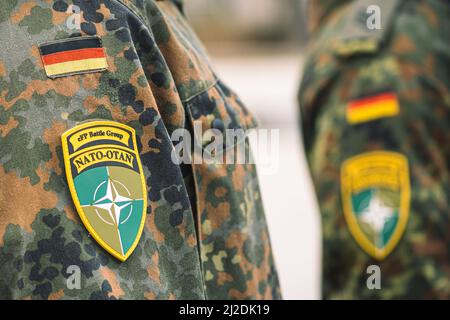 Flagge Deutschlands und Symbol der NATO-Kampfgruppe auf Soldatenuniform mit Schrotflinte oder Gewehr, NATO-Einheit zur Integration, Nahaufnahme Stockfoto