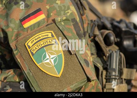 Flagge Deutschlands und Symbol der NATO-Kampfgruppe auf Soldatenuniform mit Schrotflinte oder Gewehr, NATO-Einheit zur Integration, Nahaufnahme Stockfoto