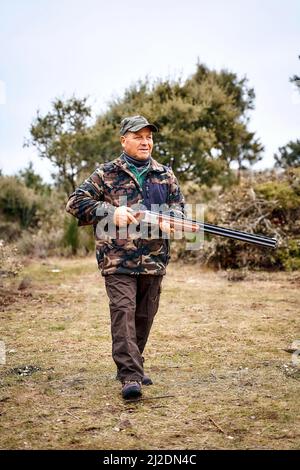 Ganzkörperjäger in Camouflage-Oberbekleidung und Mütze mit einer Waffe, die zum Schießen bereit ist Stockfoto