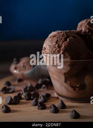 Schokoladeneis in einem Glas mit Schokoladenstückchen an der Seite und dunkelblauem Hintergrund Stockfoto