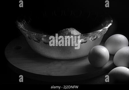 Schwarz-Weiß-Fotografie Konzept der Backen in einer Küche mit einer Schüssel aus Mehl und Eiern auf einem Schneidebrett, Stillleben Fotografie Stockfoto