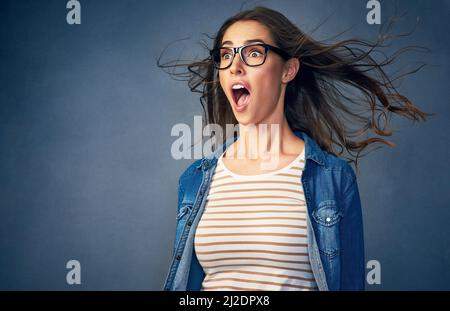 Überraschung. Aufnahme einer glücklichen jungen Frau mit Luft, die ihr im Studio ins Gesicht geblasen wurde. Stockfoto