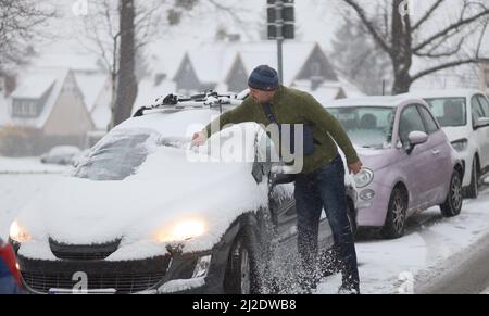 Wernigerode, Deutschland. 01. April 2022. Ein Mann schiebt Schnee von seinem Auto. Glatte Straßen verursachten am Morgen Verkehrsbehinderungen. Bis in die Tiefebene gibt es in der Region Schnee. Weitere Schneeschauer werden in den kommenden Tagen erwartet. Quelle: Matthias Bein/dpa/Alamy Live News Stockfoto