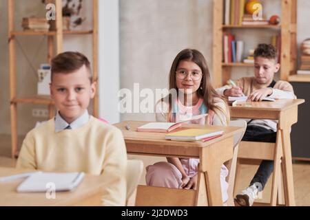 Porträt von niedlichen Schulmädchen tragen Brille und hören Lehrer, während am Schreibtisch im Klassenzimmer sitzen, kopieren Raum Stockfoto