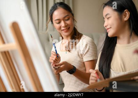 Porträt zweier asiatischer Schwestern, die Spaß und Freude haben, malen und zeichnen auf einer Leinwand mit Wasserfarbe zusammen. Stockfoto