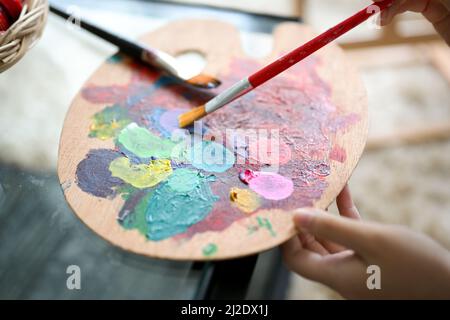 Nahaufnahme, Eine junge Frau, die eine Acrylfarbe in der Hand hält und die Farbe mit ihrem Pinsel mischt. Stockfoto