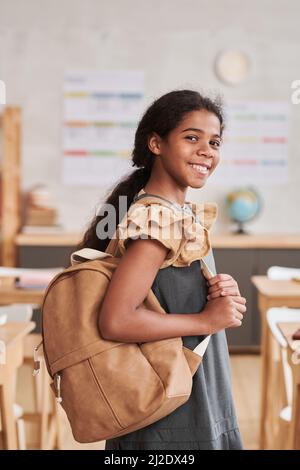 Vertikales Porträt eines lächelnden afroamerikanischen Mädchens in der Schule, das im Klassenzimmer auf die Kamera schaut Stockfoto