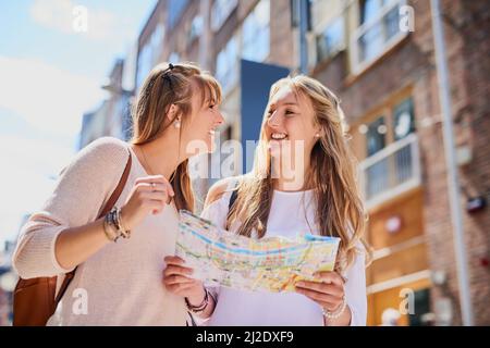 Wir sollten uns besser nicht verlaufen. Low-Angle-Aufnahme von zwei attraktiven jungen Freundinnen, die eine Karte lesen, während sie eine fremde Stadt erkunden. Stockfoto
